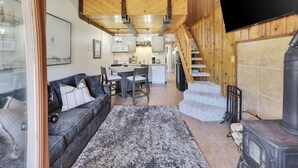 Un salon chaleureux avec une cheminée, un escalier et une cuisine en arrière-plan.