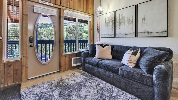 Une pièce chaleureuse avec un canapé gris foncé, un tapis à motifs et un plafond en bois.