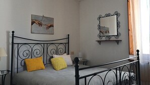 Une chambre à coucher avec un lit en métal, une table de chevet, une lampe, un miroir fixé au mur et deux tableaux.