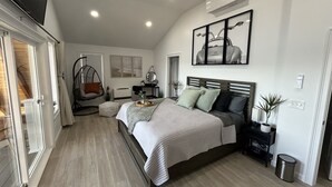A bedroom with a bed, a hanging chair, a small table, and a potted plant.