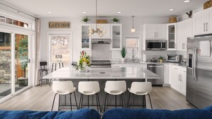 A modern kitchen with a large island, white cabinetry, stainless steel appliances, and a view of the outdoors.