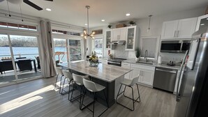 A modern kitchen with a large island, white cabinetry, stainless steel appliances, and a view of a lake.
