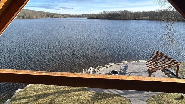 A view from a wooden balcony overlooking a lake, with a bench and a paved area in the foreground.