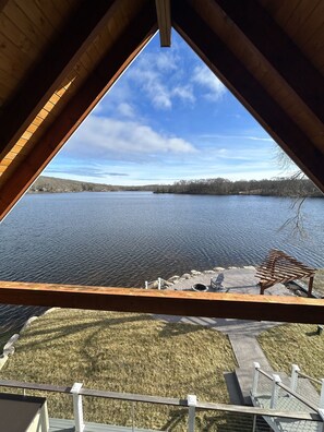 A view from a wooden balcony overlooking a lake, with a bench and a paved area in the foreground. - New contemporary lakefront home 8 min from Casinos with fun water activities! (Preston)