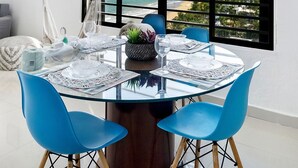 Un comedor con mesa de vidrio, sillas azules y vistas al océano y edificios.