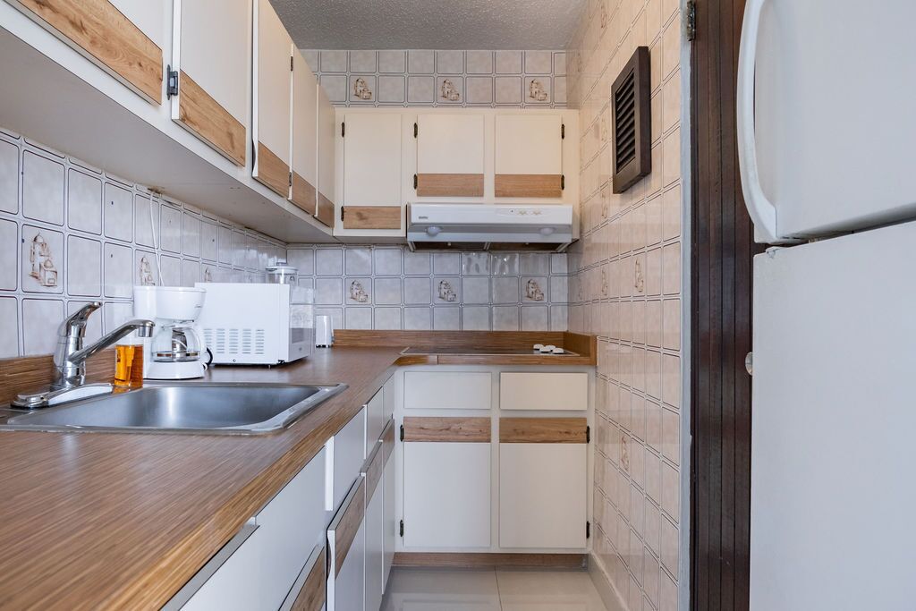 A compact kitchen with white cabinets, a stainless steel sink, and a coffee maker.