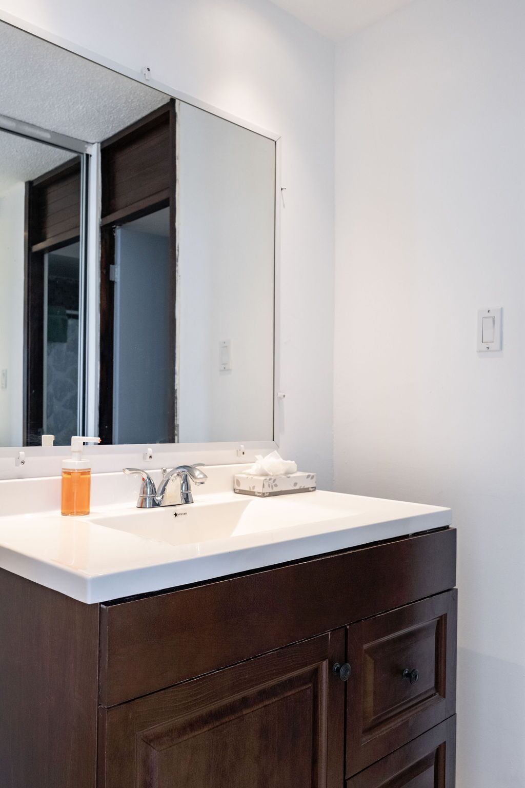 A bathroom with a white sink, a large mirror, and dark wooden cabinetry.