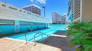 Piscina exterior con un elemento acuático azul, rodeada por una terraza de concreto y palmeras.