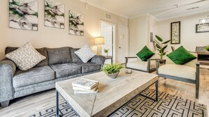 A modern living room with a grey sofa, a coffee table with books, and a green plant. - 10 Mi to Disney! Resort Condo at ChampionsGate (Davenport)