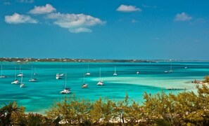 A coastal view with multiple sailboats anchored in turquoise waters, surrounded by greenery and a clear sky. - Newly Remodeled Hillside Unit at the Hideaways (Exuma)