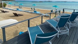Une terrasse au bord de la plage, dotée de chaises longues et de parasols, d’où l’on peut admirer une mer calme et des îles lointaines.