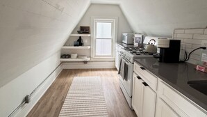 A small, white-walled kitchen with a sloped ceiling, a window, and a built-in stove.