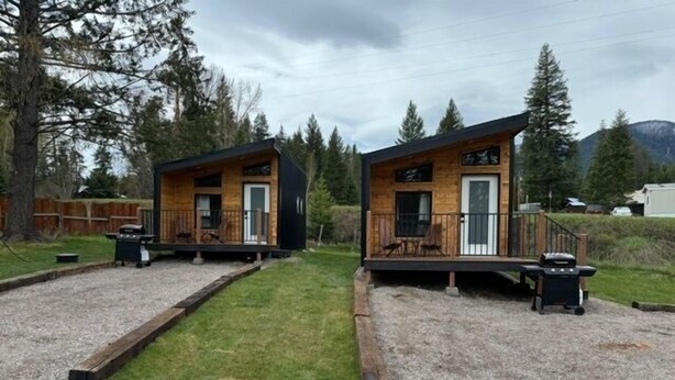 Dos cabañas de madera con terrazas separadas, cada una con una parrilla y mobiliario exterior.
