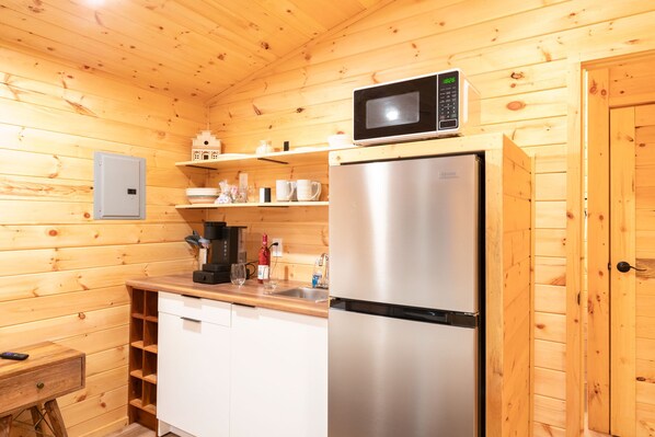 Una cocina compacta con paredes de madera, un refrigerador de acero inoxidable, un microondas y una cafetera.