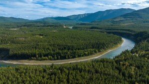 Une rivière serpente à travers une vallée densément boisée, avec des montagnes en arrière-plan.