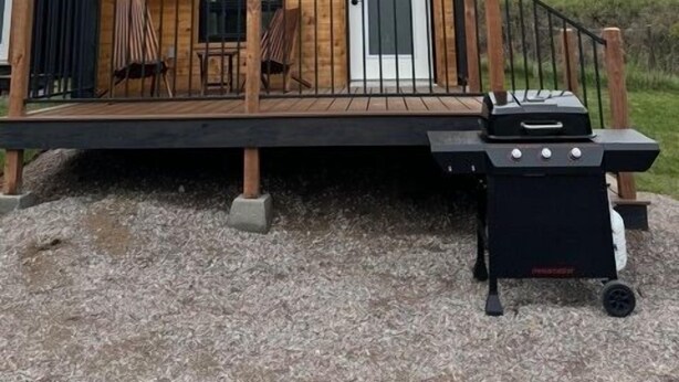Une cabane moderne dotée d’une terrasse, d’un barbecue et d’une porte avec une fenêtre.