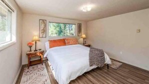 Een slaapkamer met een bed, twee nachtkastjes, een raam en een bijzettafeltje.