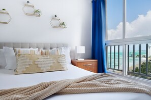 Un dormitorio con cama, mesitas de noche, una ventana con vista a la playa y decoraciones hexagonales en la pared.