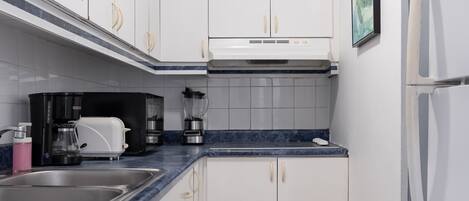 Una cocina compacta con armarios blancos, encimera azul, cafetera y refrigerador.