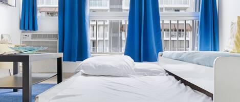A hotel room with two beds, a table, and a window with blue curtains.