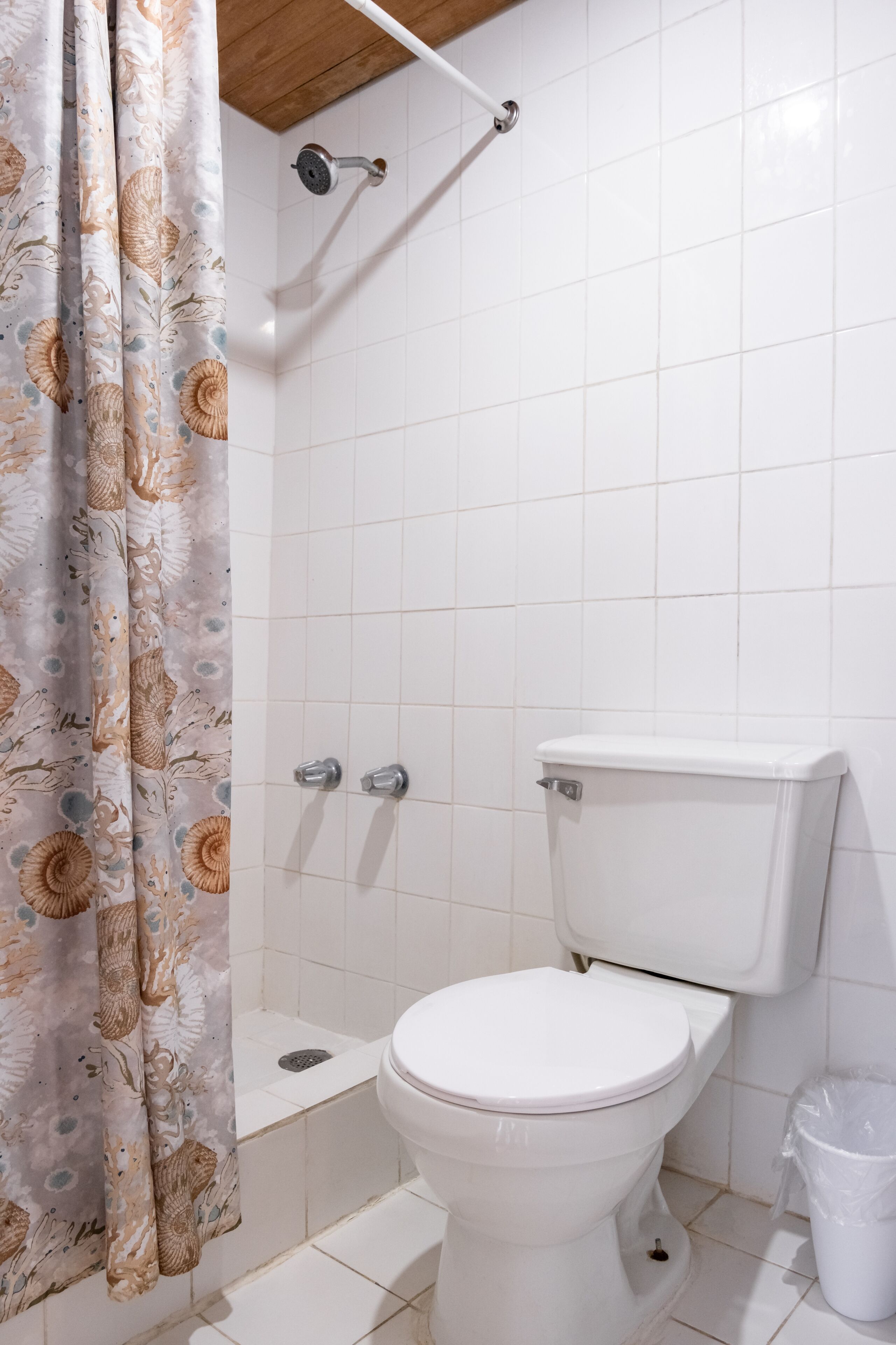Un baño con inodoro, ducha y cortina decorada con motivos florales.