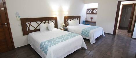 A hotel room with two beds, a wooden headboard, a nightstand with a lamp, and a small table with a vase.