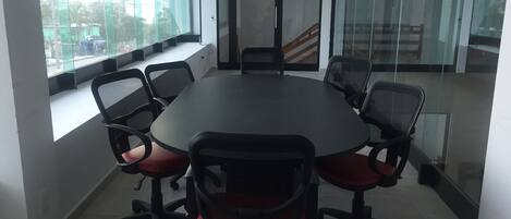 A conference room with a round table, six chairs, and large windows.