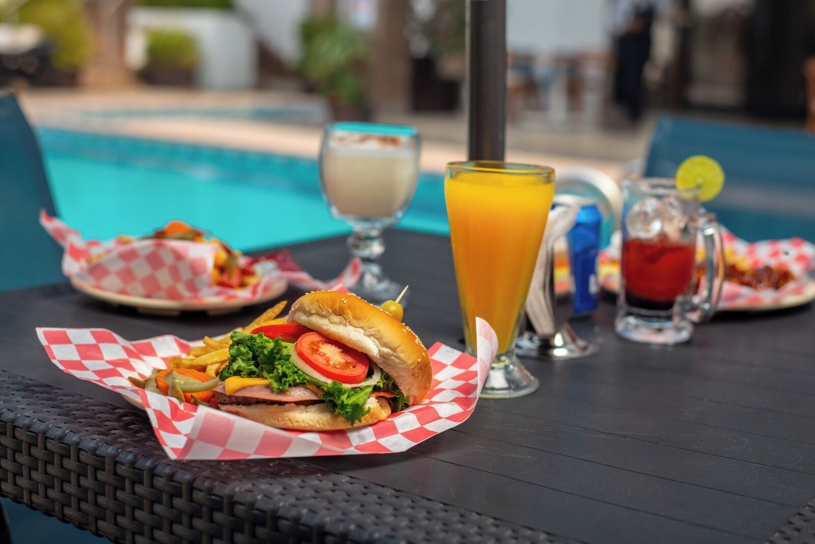 A table with a burger, a glass of orange juice, and a drink with a lemon slice.