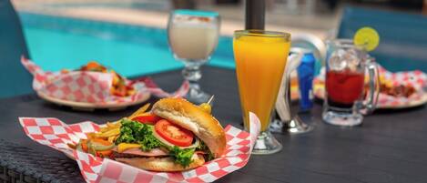 A table with a burger, a glass of orange juice, and a drink with a lemon slice.