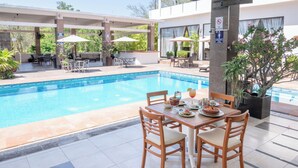 Ein Essbereich am Pool mit einem für zwei Personen gedeckten Tisch, umgeben von Stühlen, und einem Pool im Hintergrund.