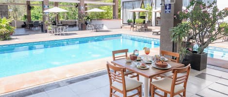 Zona de comedor junto a la piscina con una mesa dispuesta para dos personas, sillas alrededor y una piscina al fondo.