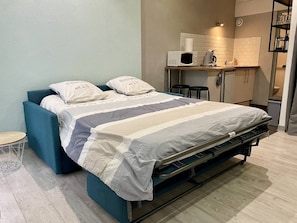 Un dormitorio pequeño con cama, una mesita, microondas y kitchenette.