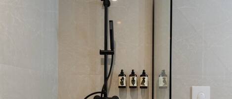 A modern bathroom with a glass-enclosed shower, a white toilet, and a wall-mounted control panel with multiple shower heads.