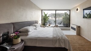 A modern bedroom with a large bed, a telephone, a small table with flowers, and a balcony with chairs and plants. - Regal Hotel Mitropoleos (Athens)