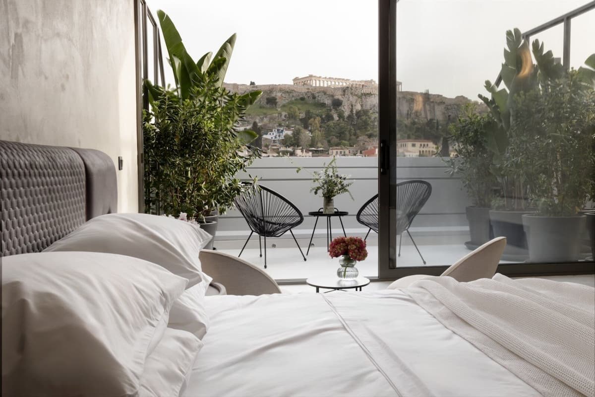 A bedroom with a bed, two chairs, a small table with a vase, and a view of a historic building.