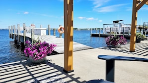 A wooden pier with a lifebuoy, a bench, and potted flowers. - Lakefront cottage on Muskegon Lake! Fire pit, 40' BOAT DOCK, near beach, shops (Muskegon)