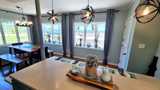 A spacious kitchen with a large island, modern pendant lights, and a view of the outdoors through large windows. - Lakefront cottage on Muskegon Lake! Fire pit, 40' BOAT DOCK, near beach, shops (Muskegon)