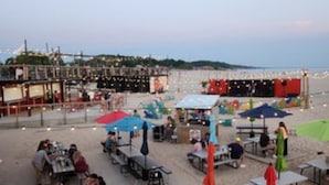 An outdoor dining area with tables and chairs, a stage, and a view of the sea. - Lakefront cottage on Muskegon Lake! Fire pit, 40' BOAT DOCK, near beach, shops (Muskegon)