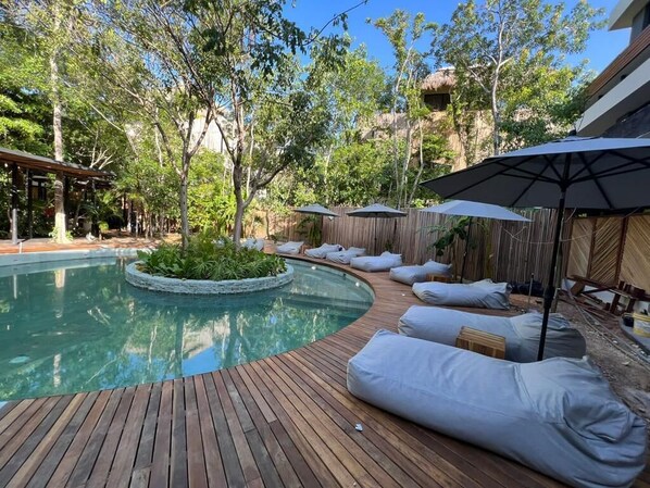 A pool area with wooden decking, lounge chairs, and umbrellas.