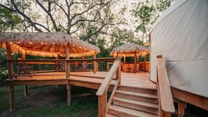 Eine Holzterrasse mit strohgedeckten Gebäuden, einem überdachten Sitzbereich und einem Zelt.