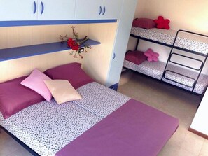 A bedroom with a bunk bed, a bed with patterned bedding, and a shelf with flowers. - Fully Furnished Apartment on the top Floor (San Michele al Tagliamento)