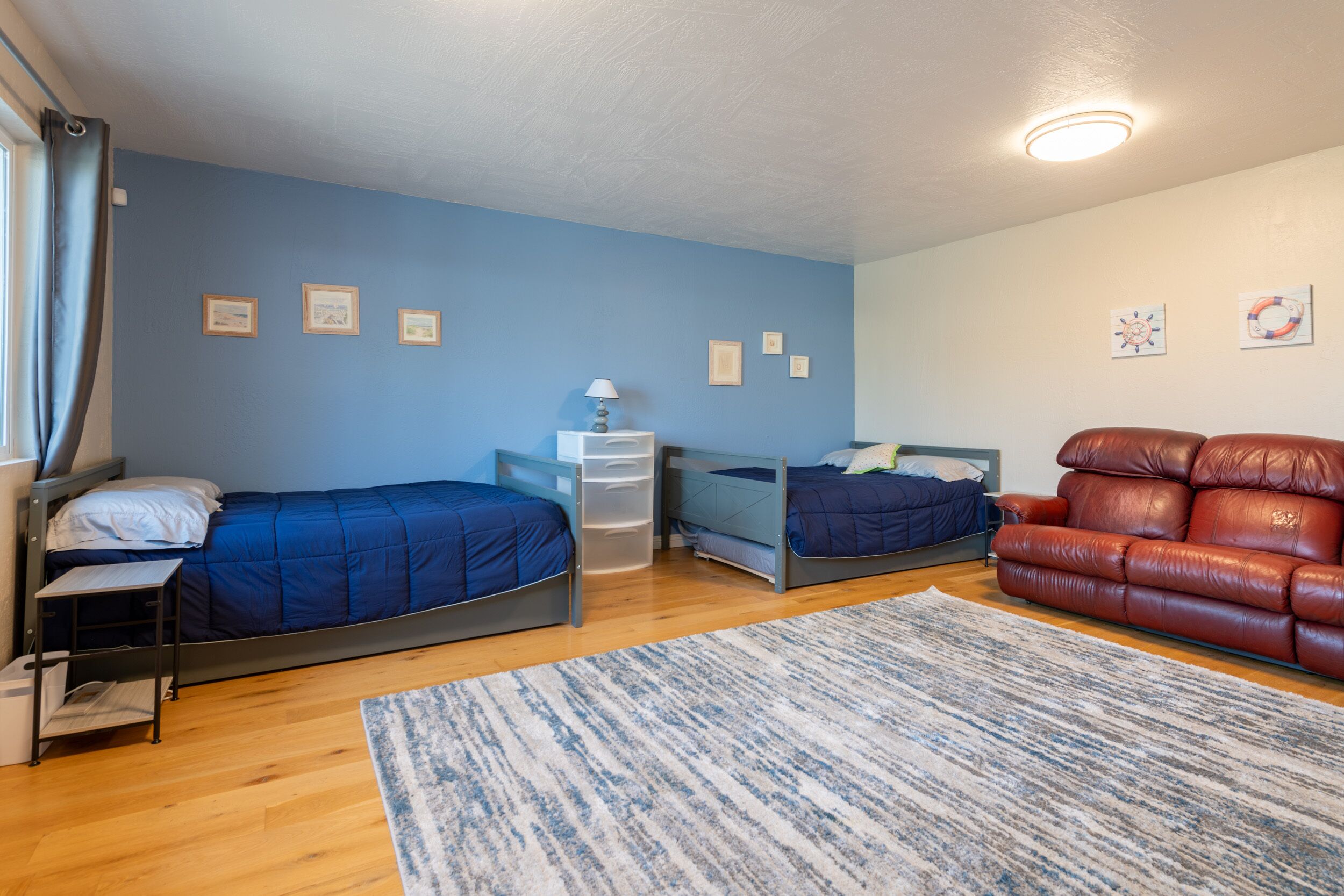 A bedroom with two beds, a desk, a red leather sofa, and a blue wall.