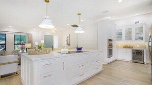 A modern kitchen with white cabinetry, a central island, pendant lighting, and a view of the living area.