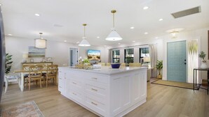 A spacious kitchen with a central island, pendant lighting, and a dining area with wooden chairs and a table.