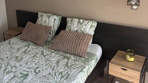 A bedroom with a bed, nightstands, a wall-mounted lamp, and a power strip. - Village Camarguais Logement 4 Personnes (Arles)