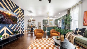 A modern living room with a checkered rug, two orange armchairs, a green sofa, and a dining area with a table and chairs. - Mntn & Asheville Views! Movie Theater! Game Rm! Hot Tub! Fire Pit! Pets Welcome! (Candler)