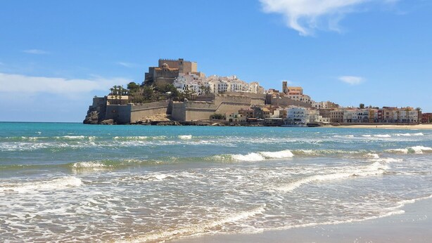 Un pueblo costero con una estructura imponente similar a un castillo en una colina, con vista al mar.