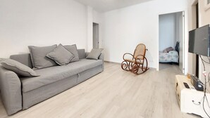 Una sala de estar moderna con un sofá gris, un sillón mecedor de mimbre y un televisor de pantalla plana.