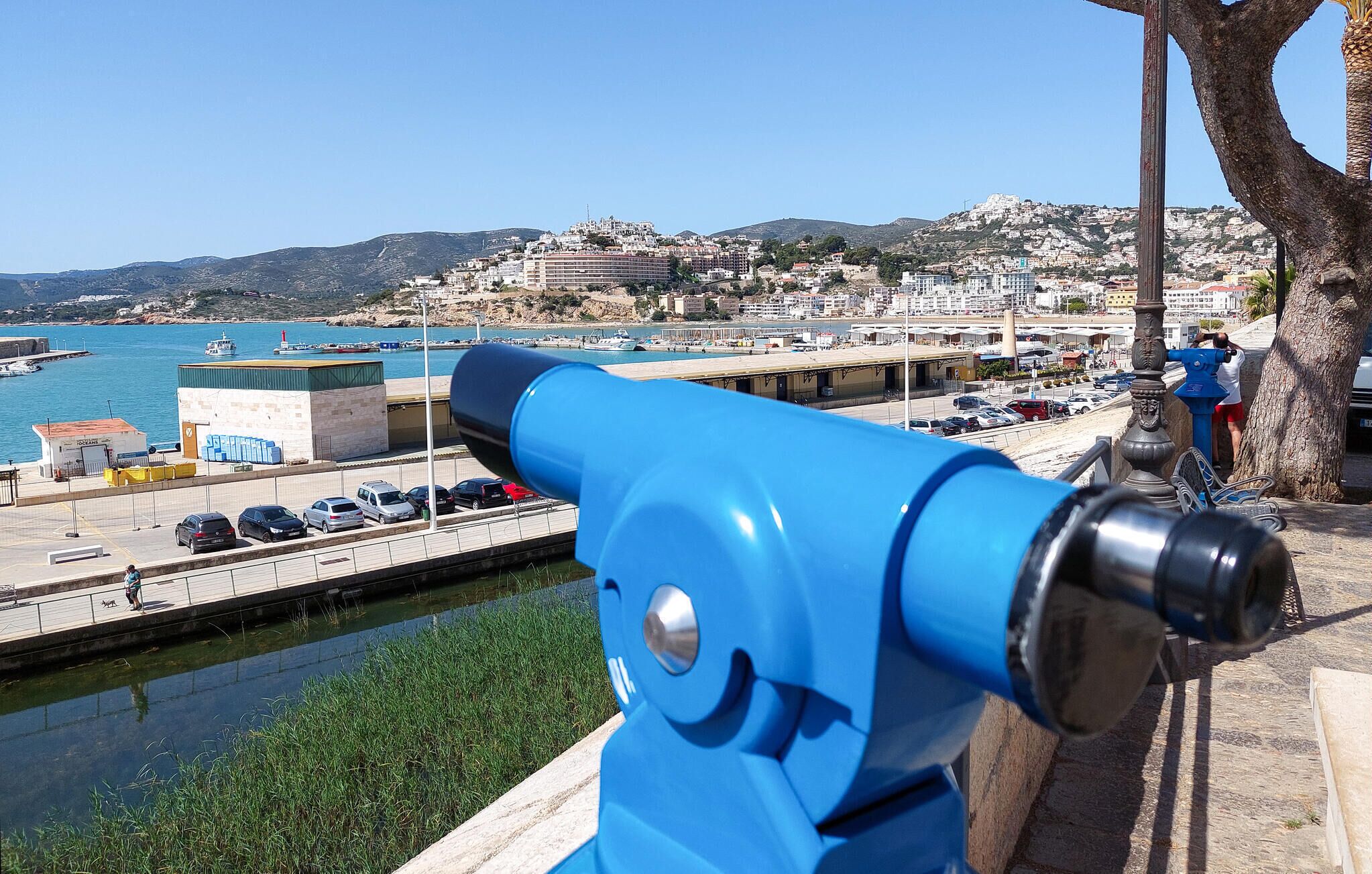 A blue telescope overlooking a harbor with buildings and a clear sky.