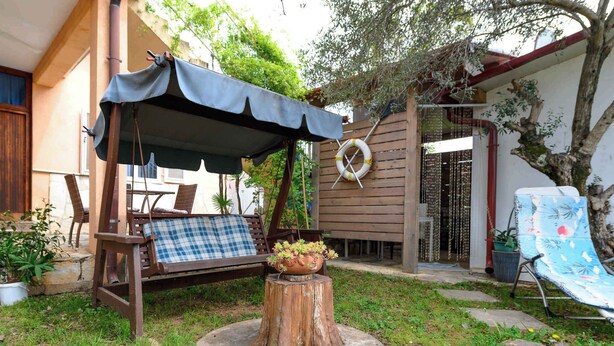 A wooden deck with a swing chair, a covered seating area, and a wooden stump with a flower pot. - Holiday apartment Cheap accommodation in a great location (Bašanija)